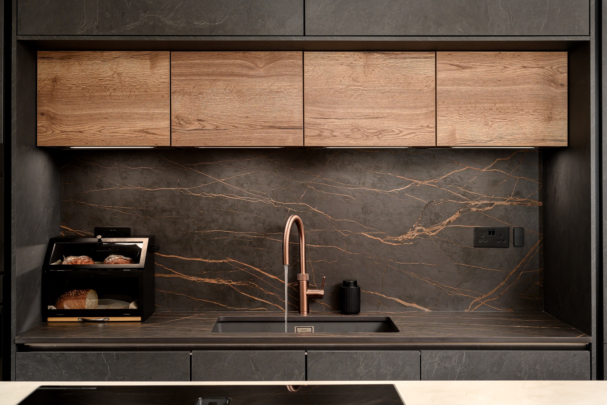 The sink and dark stone splashback at Chiswick House, with fine copper-toned veining and a copper tap