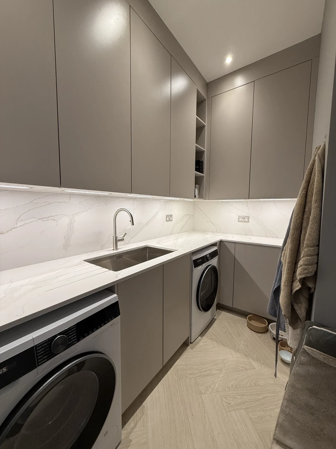 Utility room with Sand-painted cabinetry, tall wall units, laundry appliances and an illuminated sink area