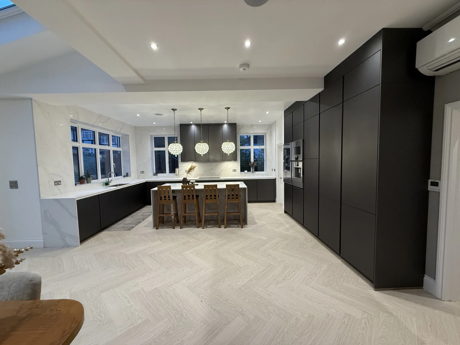 Full view of the Ealing kitchen showing tall cabinetry, island seating and wall cladding
