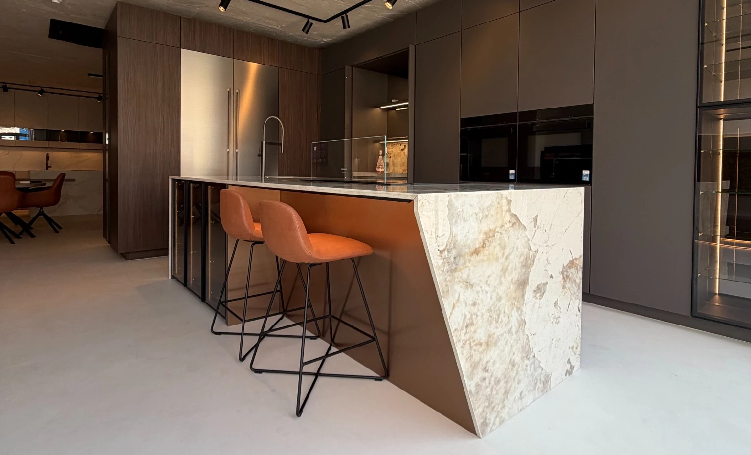 Sculpted stone island with orange stools and dark contemporary cabinetry